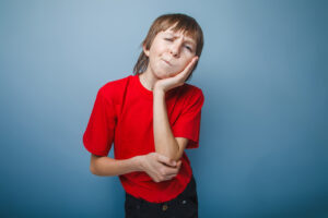 boy teenager European appearance in a red shirt a hand to his cheek against the gray background, toothache
