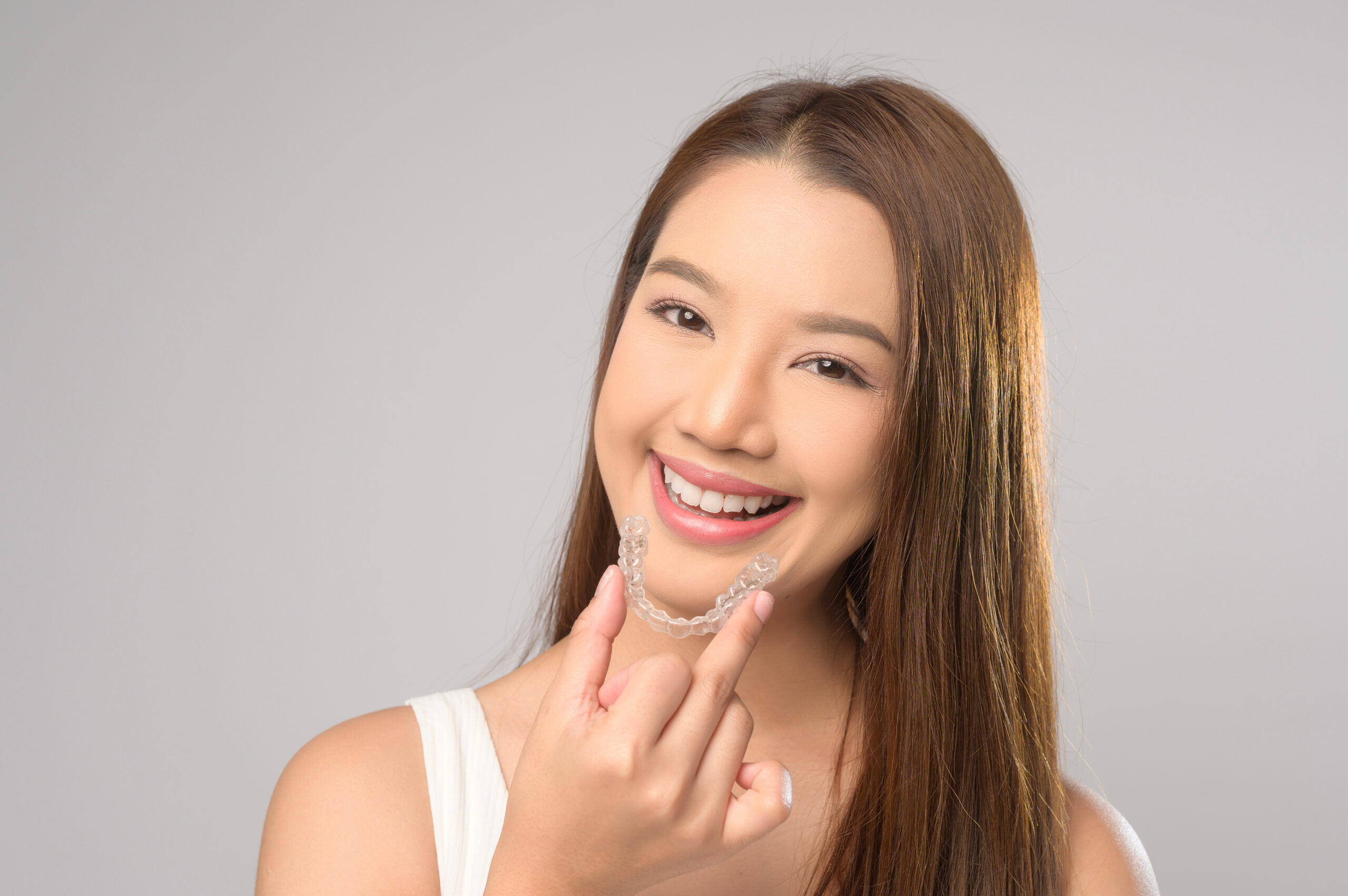 A Young smiling woman holding invisalign braces over white background studio, dental healthcare and Orthodontic concept.