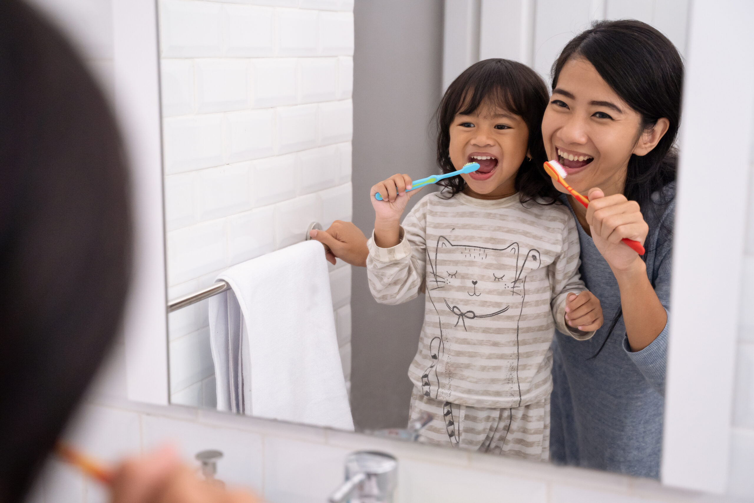 happy attractive mom and kid brushing their teeth together in bathroom sink in the morning